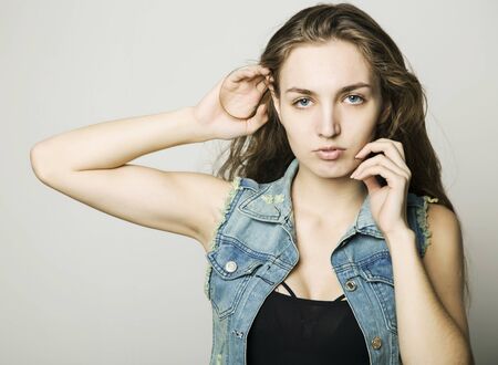 young beautiful happy stylish hipster girl in a denim jacket and shorts posing on a light backgroundの写真素材