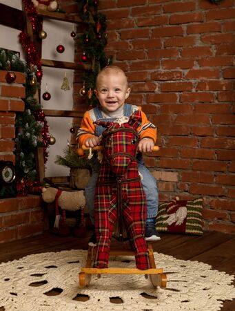 Little baby boy on rocking horse, dressed in sweater and jeans. Christmas or New Year decorationsの写真素材
