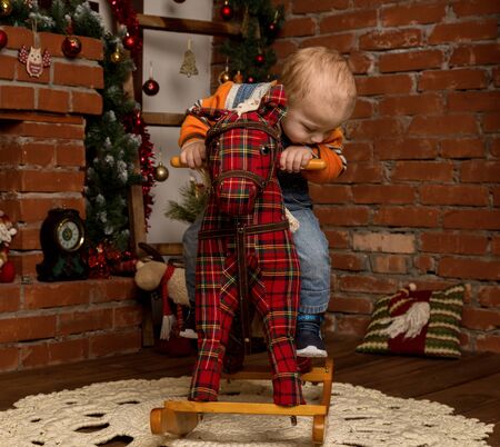 Little baby boy on rocking horse, dressed in sweater and jeans. Christmas or New Year decorationsの写真素材