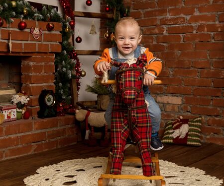Little baby boy on rocking horse, dressed in sweater and jeans. Christmas or New Year decorationsの写真素材