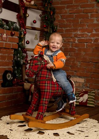 Little baby boy on rocking horse, dressed in sweater and jeans. Christmas or New Year decorationsの写真素材