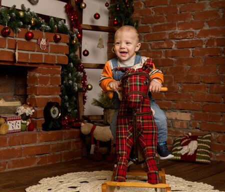 Little baby boy on rocking horse, dressed in sweater and jeans. Christmas or New Year decorationsの写真素材