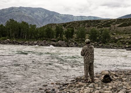 single fisherman on a stormy river is fishing on a sunny summer dayの写真素材