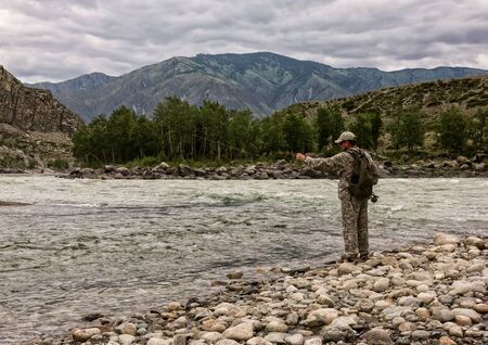 single fisherman on a stormy river is fishing on a sunny summer dayの写真素材