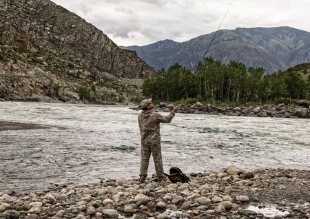 single fisherman on a stormy river is fishing on a sunny summer dayの写真素材