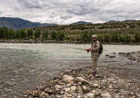 single fisherman on a stormy river is fishing on a sunny summer dayの写真素材