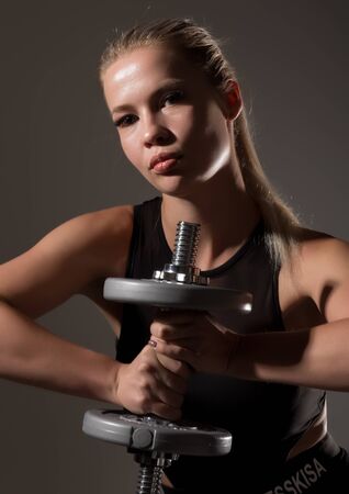 Fitness sexy girl with dumbbells on a dark background. Athlete doing exercises in the gymの写真素材