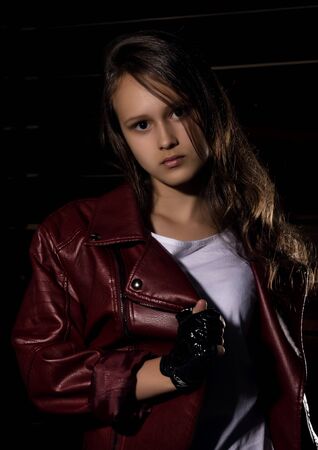 Beautyful Girl in leather jacket in a dark. Mysterious disobedient child, problems with early growing girlsの写真素材