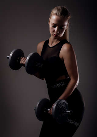 Fitness sexy girl with dumbbells on a dark background. Athlete doing exercises in the gymの写真素材