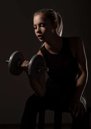 Fitness sexy girl with dumbbells on a dark background. Athlete doing exercises in the gymの写真素材