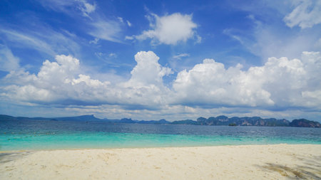 Beach featuring pristine white sands, a calm turquoise ocean, and a sunlit sky of fluffy clouds. Beach and sea with blue sky and white cloud background.の写真素材