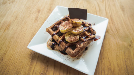 Breakfast waffles with bananas and chocolate sauce. Traditional waffles with fresh banana and Chocolate sauce. Wood background. Top viewの写真素材