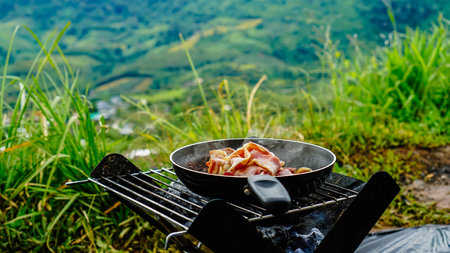 Slices of fried bacon in a pan. Food in a forest camp. Cooking on fire. Picnic in the nature. Grilled food on nature.の写真素材
