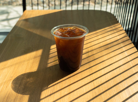Coffee with ice cubes in drinking glass on wood table background with a sunbeam from the window....