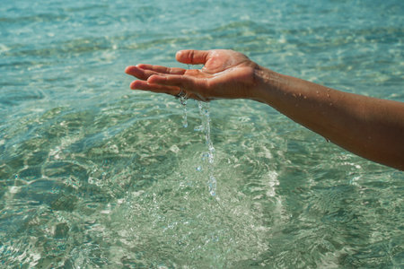 Hands with pure water. Closeup of a woman's hand touching the lake water. A person's hand reaching out to touch a rippling water surface, exploring the tactile dimension of sensory perception. A concepts of cleansing, nature, environment and sustainabilityの写真素材
