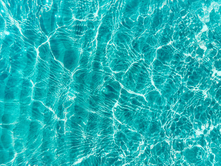 Water ripple over sandy beach. Transparent blue colored clear water surface texture with splashes....