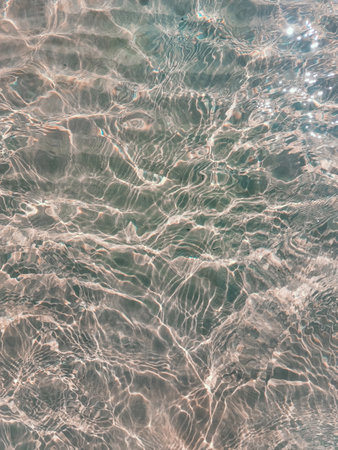 Water ripple over sandy beach. Transparent blue colored clear water surface texture with splashes....