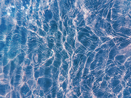 Water ripple over sandy beach. Transparent blue colored clear water surface texture with splashes....