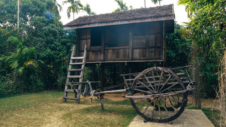 Old wooden wagons in the countryside Thailand. Old traditional Thai farmer two wheel cart with textured woven filled with dry hay during local Thai festival. Background is old Thai houses with suspended small.の写真素材