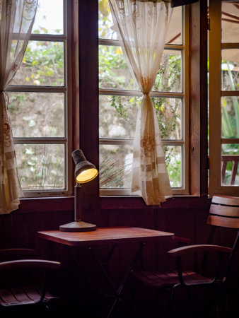 Interior of a contemporary living room with a fireplace, concrete and dark wood walls, a concrete floor, and loft windows. The sun shines through the window on the seat of the cafe.の写真素材