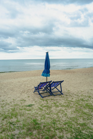 Coconut palm tree on the tropical beach with wooden beach chair and blue parasol and blue sea background. Chair, umbrella and palm tree at beautiful tropical beach. Copy spaceの写真素材
