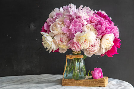 Bouquet of white, pink peonies in a vase on the table. Old vintage rustic book, black background and white tablecloth.の写真素材