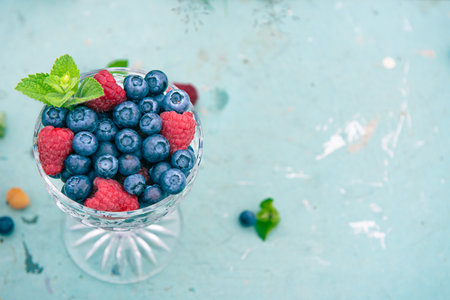 Blueberries and raspberries in a glass on a blue background. Mockup with free copy space.の写真素材