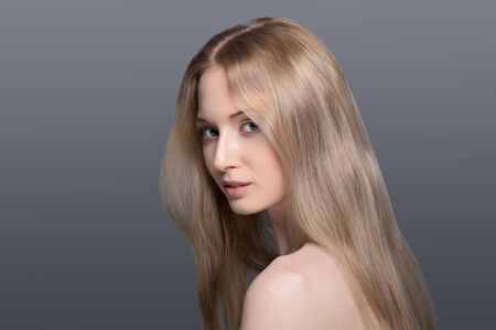 Confident in her abilities. Smiling young blond hair woman holding hands on hips and looking at camera while standing isolated grey backgroundの写真素材