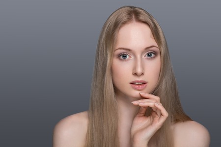 Confident in her abilities. Smiling young blond hair woman holding hands on hips and looking at camera while standing isoalted grey backgroundの写真素材