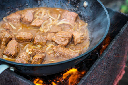 Pieces of meat fried with onions in a cauldron on fireの写真素材