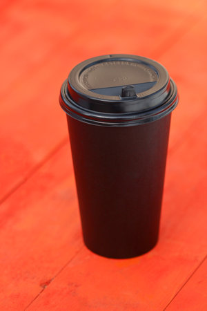 Disposable black plastic coffee cup on red wooden table