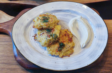 Potato pancakes with sour cream and fresh herbs on a ceramic plate. Draniki