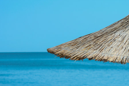 Thatched roof of a beach umbrella against the blue sea and skyの写真素材