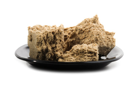 Broken pieces of halva on black porcelain saucer isolated on white backgroundの写真素材