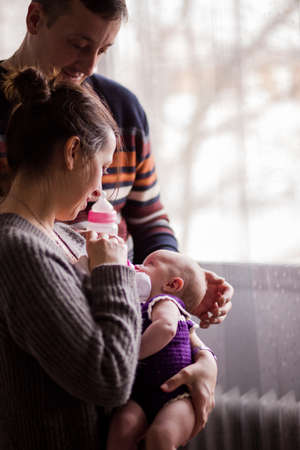 Slav Bulgarian couple with a baby. Father and mother feeding theirs firstborn daughter with a milk bottle. Fathers day and Mothers dayの写真素材