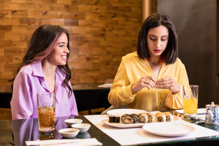 Young Hispanic woman eat sushi in a Japanese food restaurant. Lifestyle dinner for independent and confident friends taking healthy food. Yellow and lavender 2021 year colorの写真素材