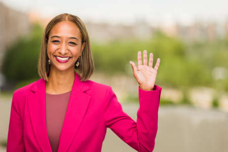Businesswoman greeting with hand waving happy and positive. south African mixed race black womanの写真素材