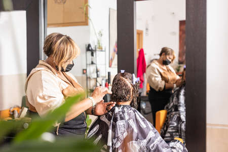 Latin small business Beauty salon. Entrepreneur hairdresser woman and mixed race client. Facemaskの写真素材