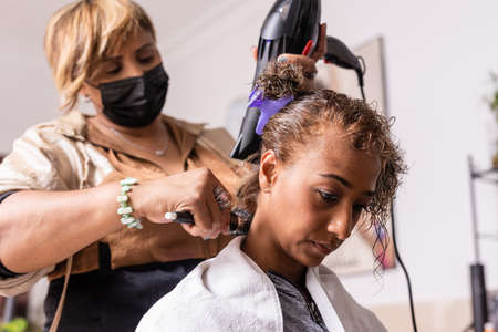 Makeover haircut in beauty salon with Latin hairdresser professional. mixed race with facemaskの写真素材