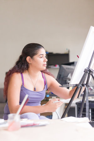 venezuelan middle aged latin woman. art hobby painting for leisure at home. cheerful apartmentの写真素材