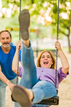 50-59 years senior happiness relationship. Hispanic family enjoy life couple with a swing in a parkの写真素材