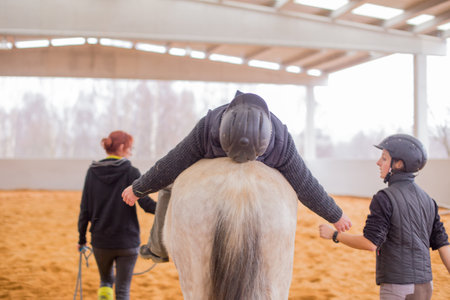 Hippotherapy assistance therapist with medical disability patient on equestrian riding hall.の写真素材