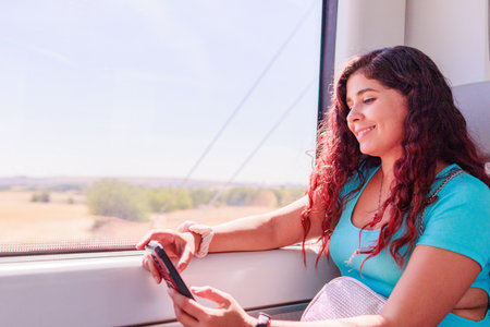 Train traveler. Hispanic mid-adult woman looking smartphone on holiday lifestyle vacationの写真素材