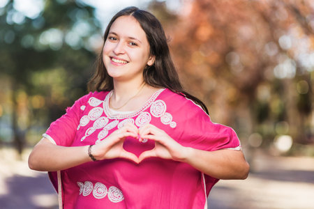 Young Moroccan woman doing heart love shape with hands with traditional dress. InspireInclusion