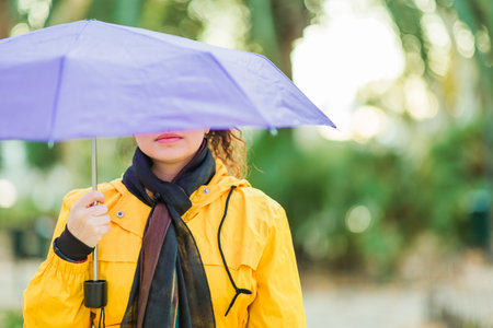 Woman holding purple umbrella wearing yellow raincoat in green parkの写真素材
