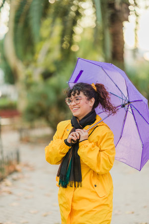 Young woman smiling and holding purple umbrella during fall rainの写真素材