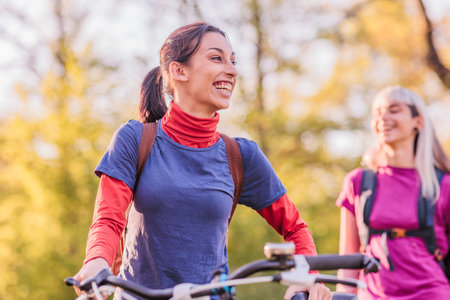 Two smiling women walking and cycling in nature during a sunny dayの写真素材