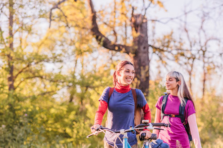 Two smiling women walking with bicycles in a forestの写真素材