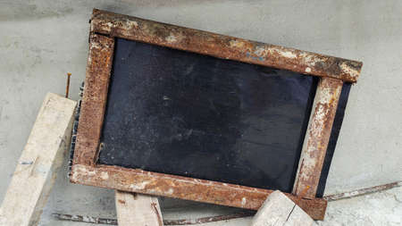 old iron picture frame against a black wooden plank background sits diagonally on a cement wall piled with scraps.の写真素材