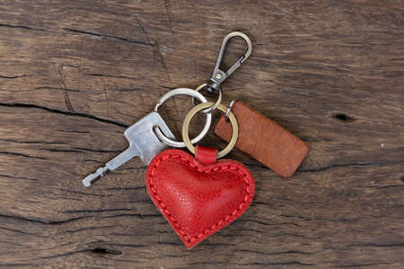 key chain is made of red heart-shaped leather. laid on old wooden floorの写真素材